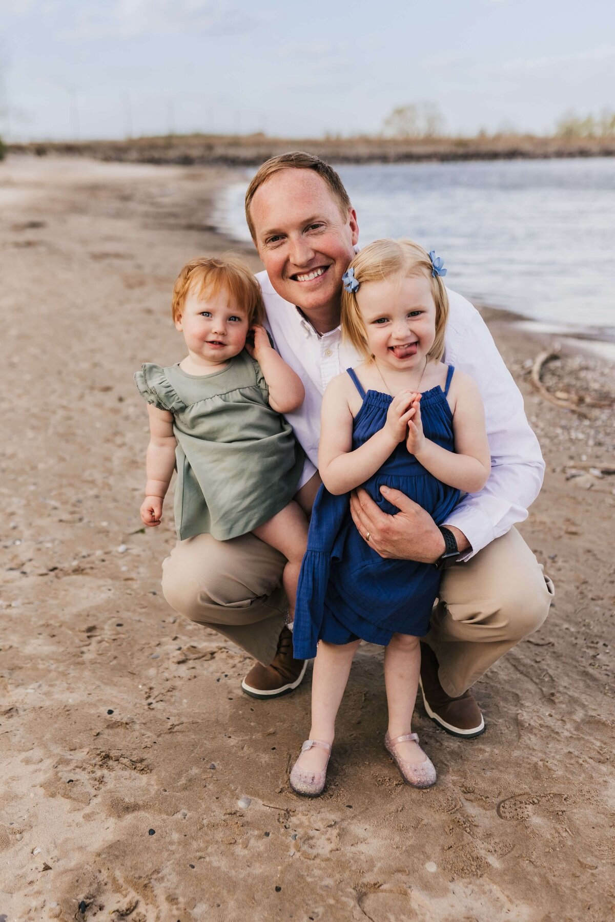 dad holding his two daughters while standing at the beach