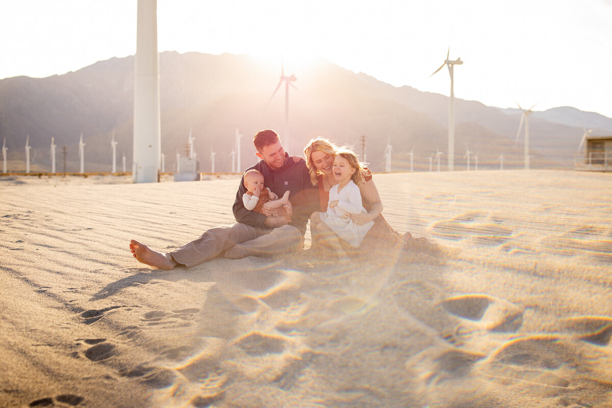 Kids laughing on parents' lap while sitting in the sand with the San Jacinto mountain range behind them. 