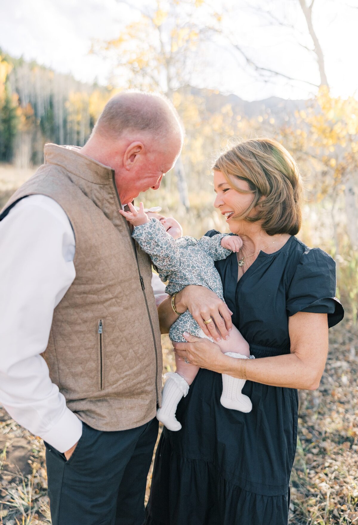 The same grandparents are cuddling with their young grandchild as she reaches up playfully for grandpas face.