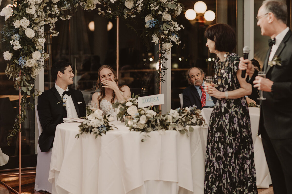 Newlyweds sitting at their reception laughing with guests 