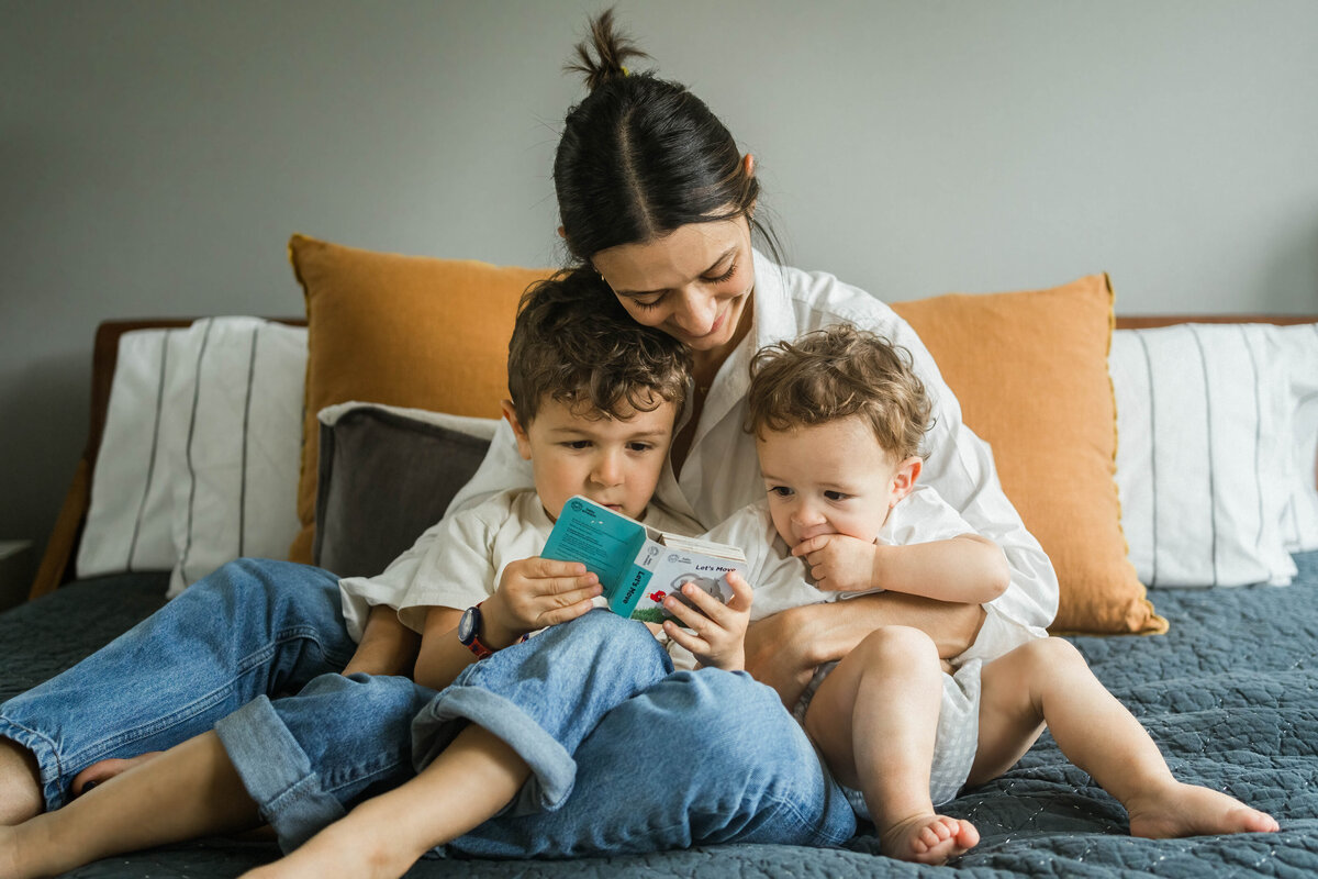 Mom and two boys sitting on bed readying a book