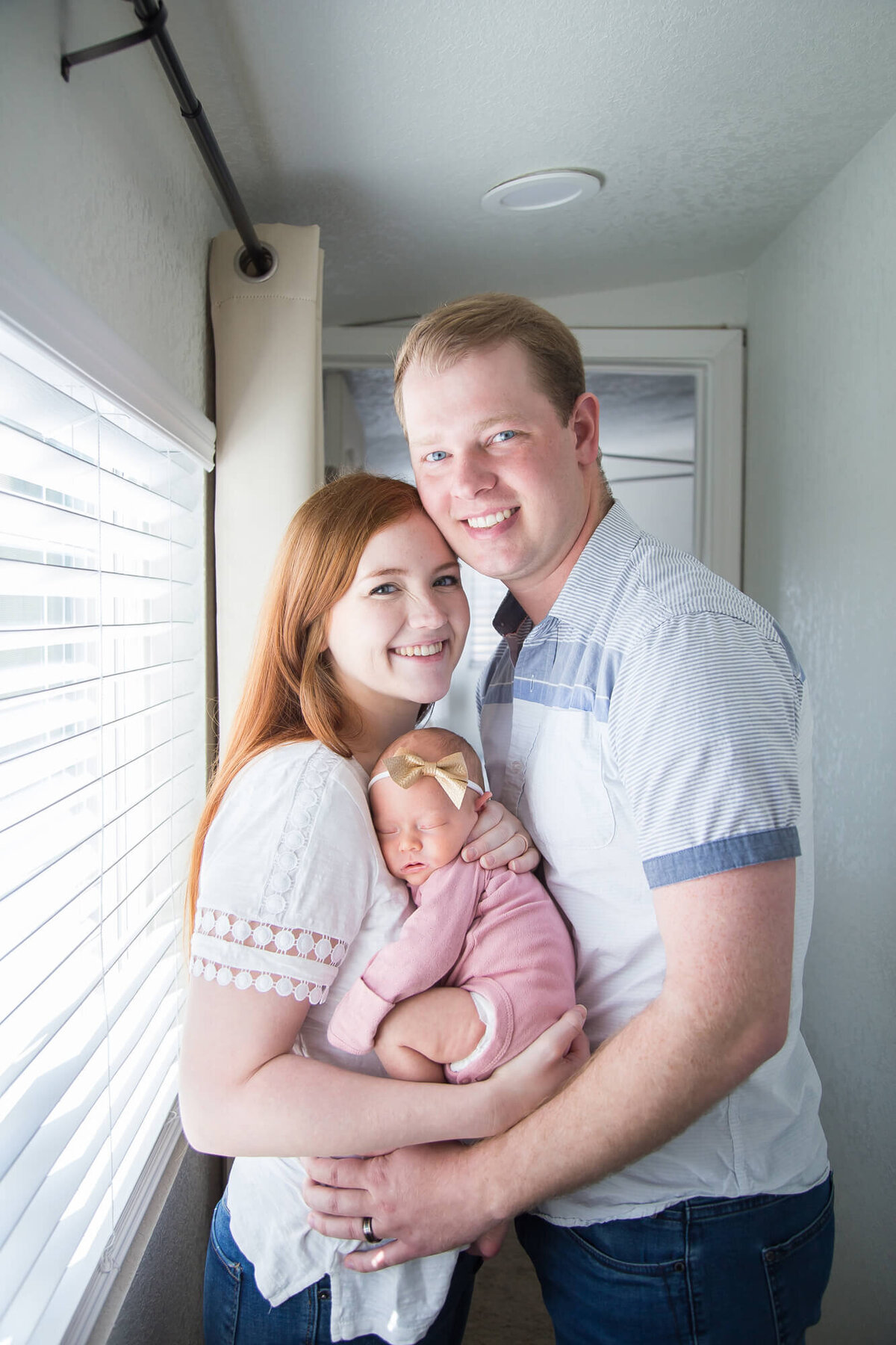 Redheaded couple standing close together with newborn baby girl between them