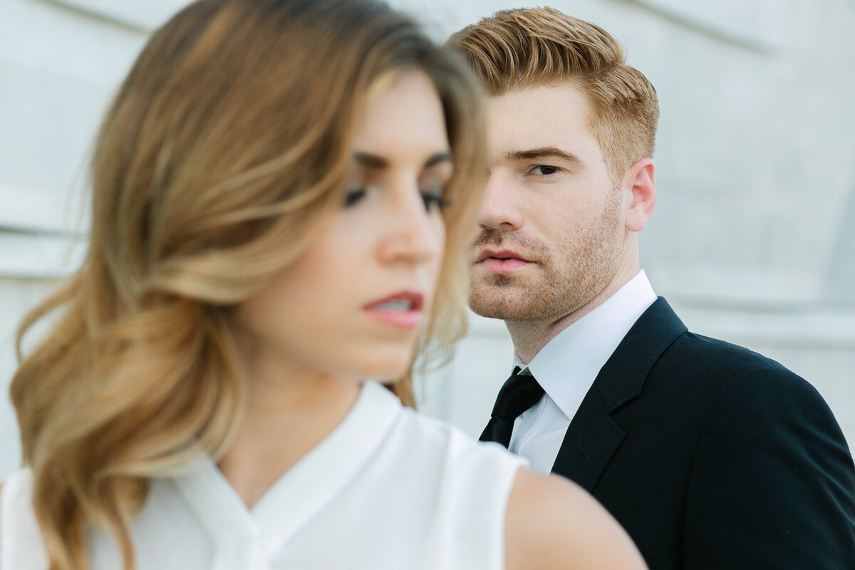 Artistic engagement portrait with the fiancé focused behind his partner who is blurred in the foreground during their engagement session.