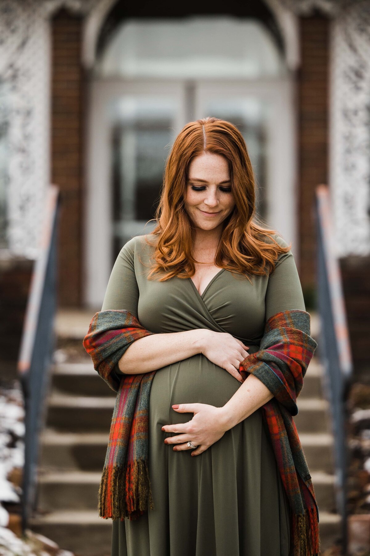 A pregnant woman holding her belly stands in front of a building, with a content expression on her face, perfectly captured by a Pittsburgh maternity photographer.
