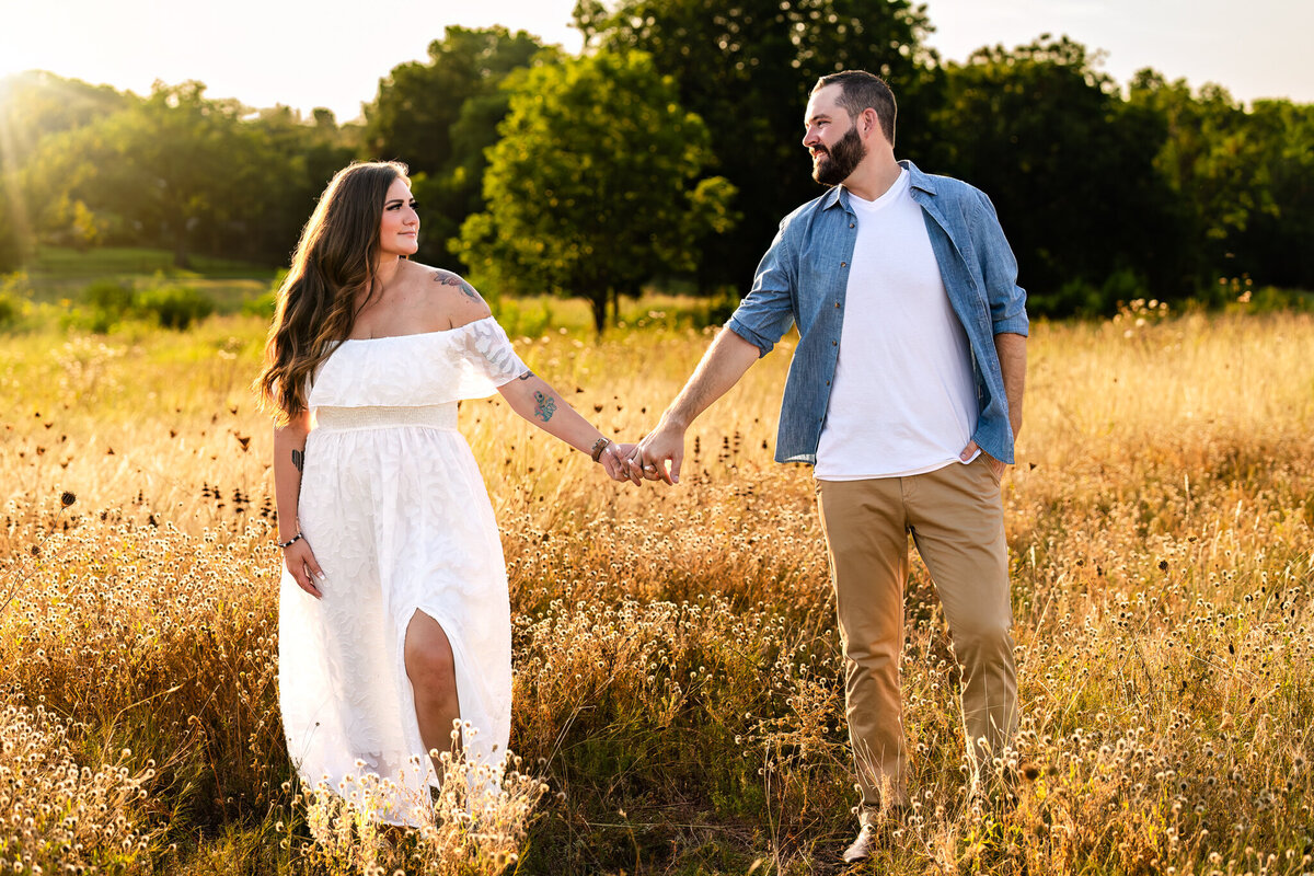 Engaged couple holding hands in a field at sunset