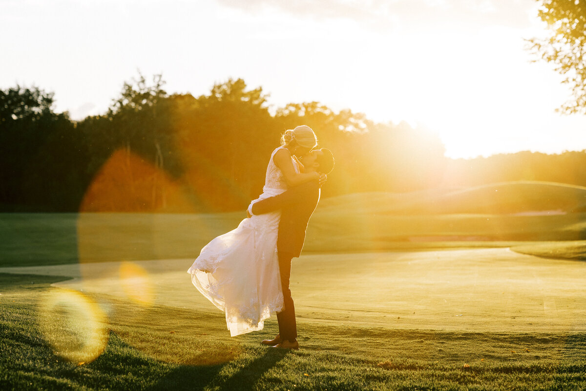 Golf course sunset with groom and bride kissing while holding her in his arms