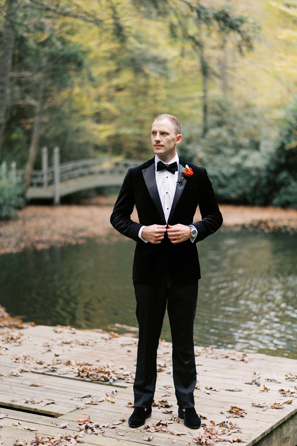 Groom in a black velvet tuxedo standing on a dock by the water at Old Edwards Inn in Highlands, North Carolina.