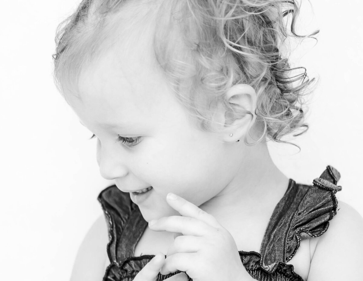 Black and white fine art portrait of toddler girl with white backdrop capturing pure expression