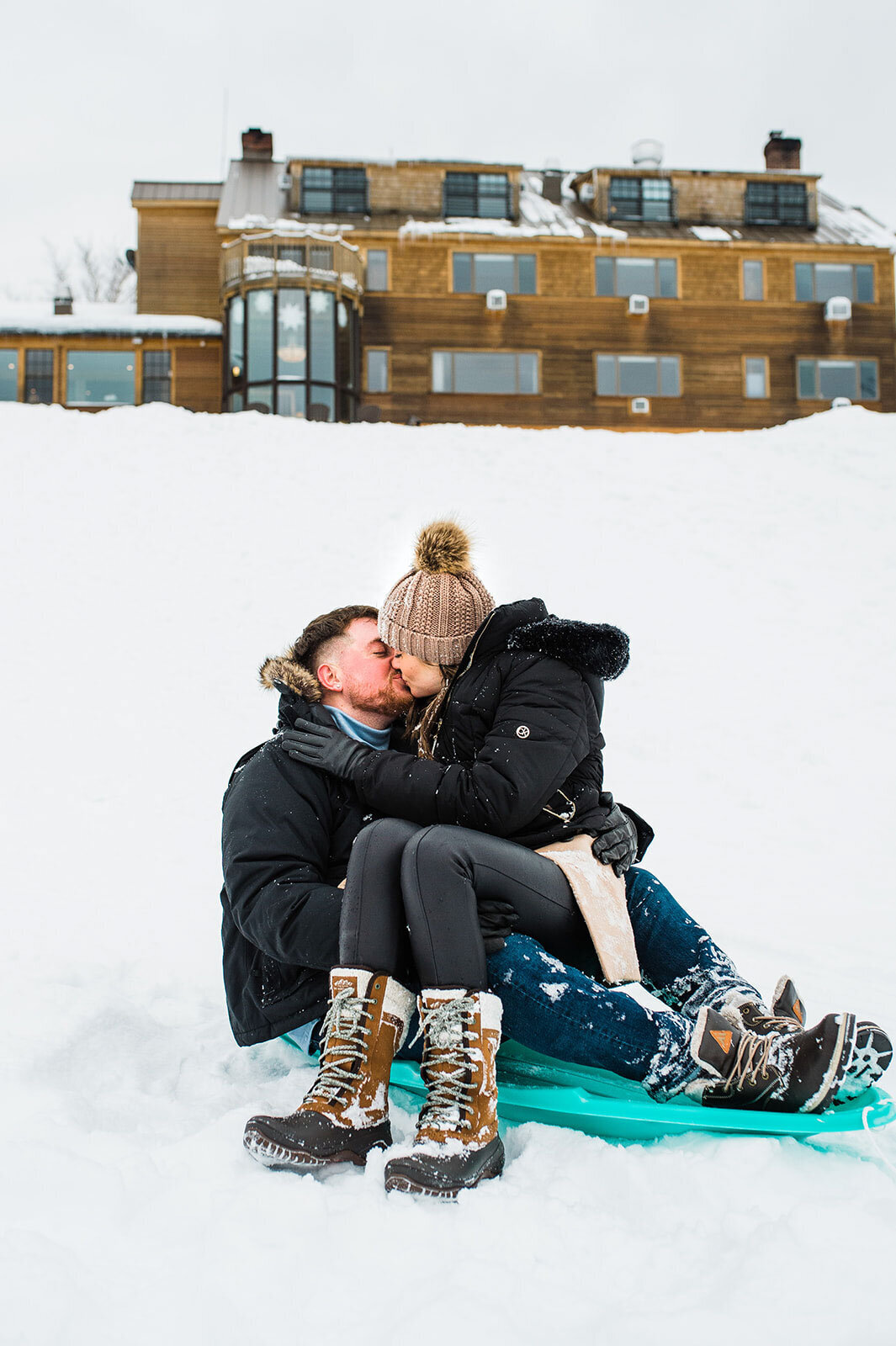 engaged couple kissing on sled at mountain top inn chittenden vermont