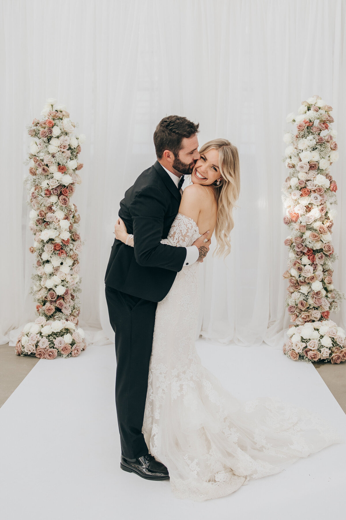 Stunning candid of bride and groom in front of luxurious pink and white rose arch