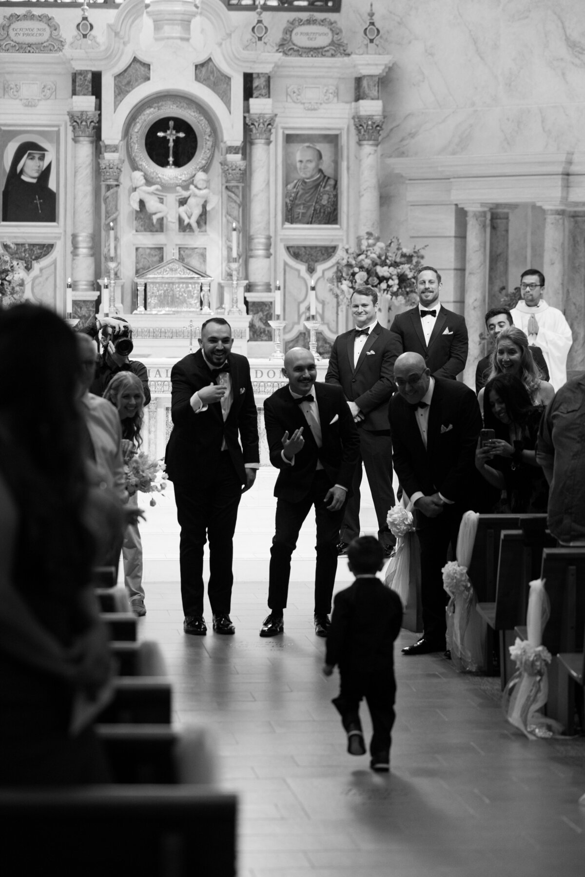 little boy running down the aisle as wedding guests cheer him on