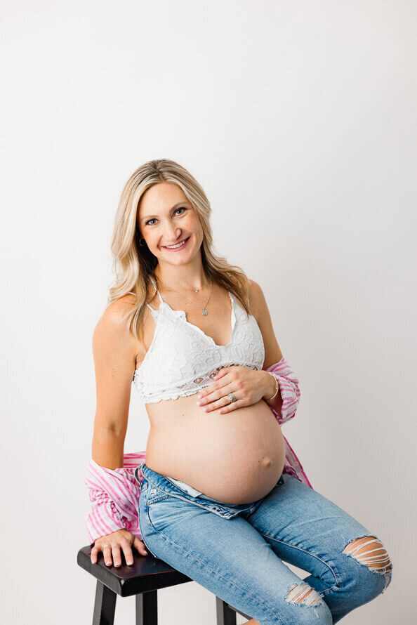 A blonde woman touches her bare pregnant belly for maternity photos.