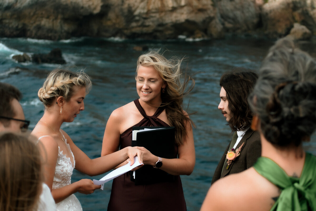 Bride and groom being married by the bride's sister surrounded by family overlooking the California ocean in Carmel by the Sea