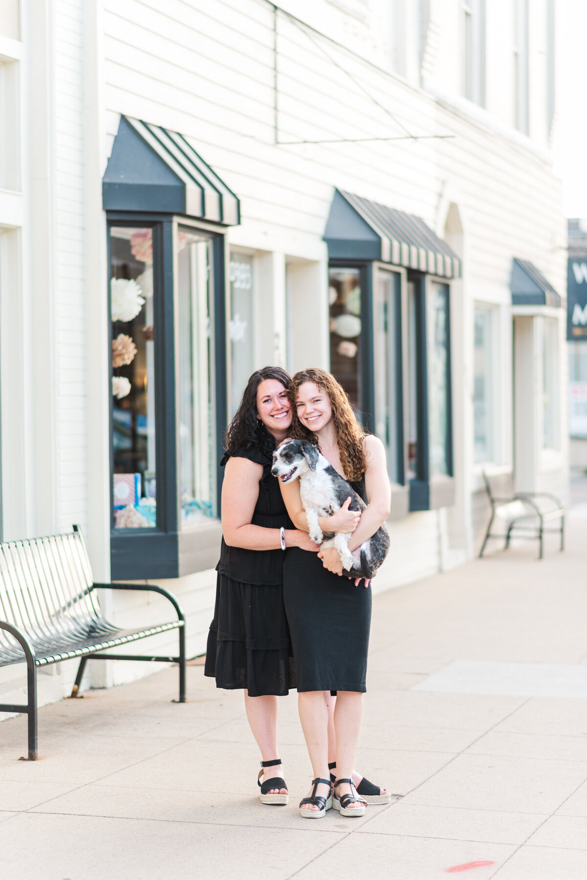 A couple, both with black dresses, walks in downtown denver with Denver wedding photographer while holding their black and white poodle pup