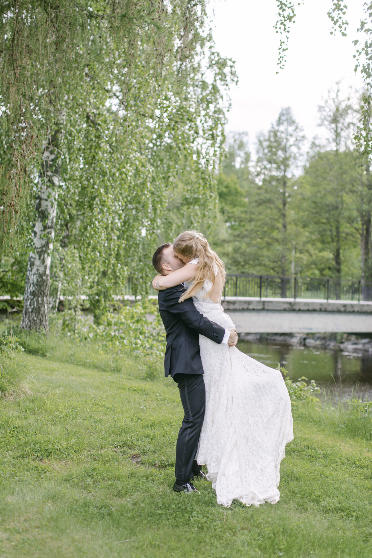 Brudgum lyfter upp bruden på en gräsmatta vid Schenströmska