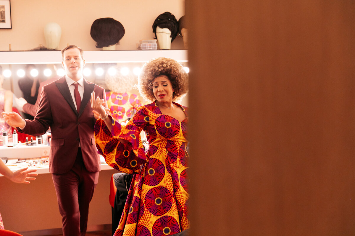 Performers in vrolijke kleren oefenen een dans in de kleedkamer van een theater.