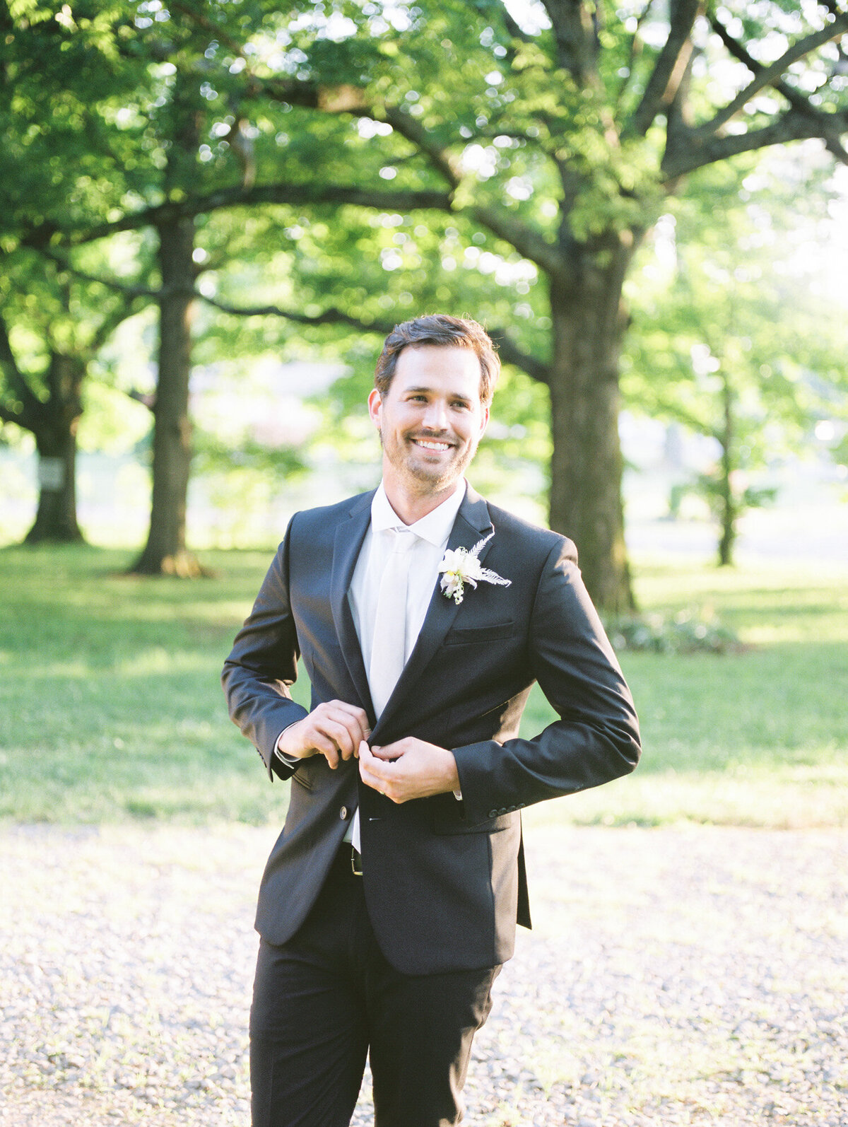 A handsome groom buttons his jacket in front of the lush greenery by Birmingham wedding photographer, Kelsey Dawn Photography