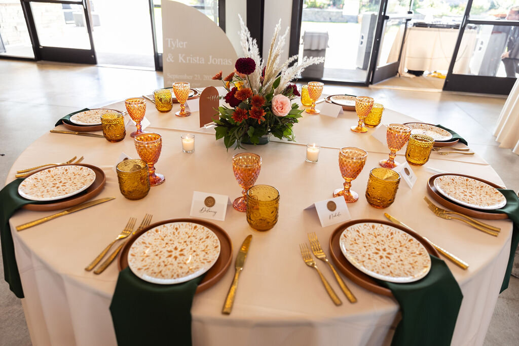 Warm fall table scape with amber cups, gold flatware and emerald napkins at Bonnie Blues Event Venue.