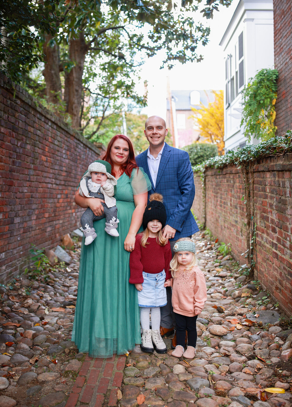 man, woman, and three children  standing on pebble and next to brick wall