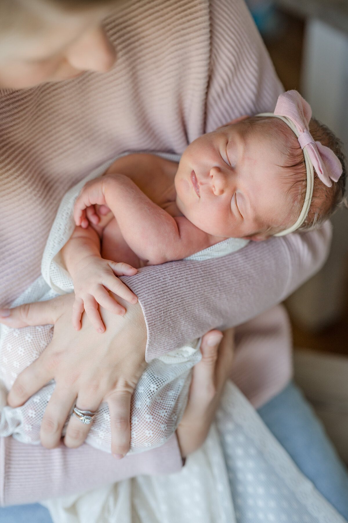 Baby girl sleeps in her mom's arm. Her tiny hand is on top of her mom's hand.