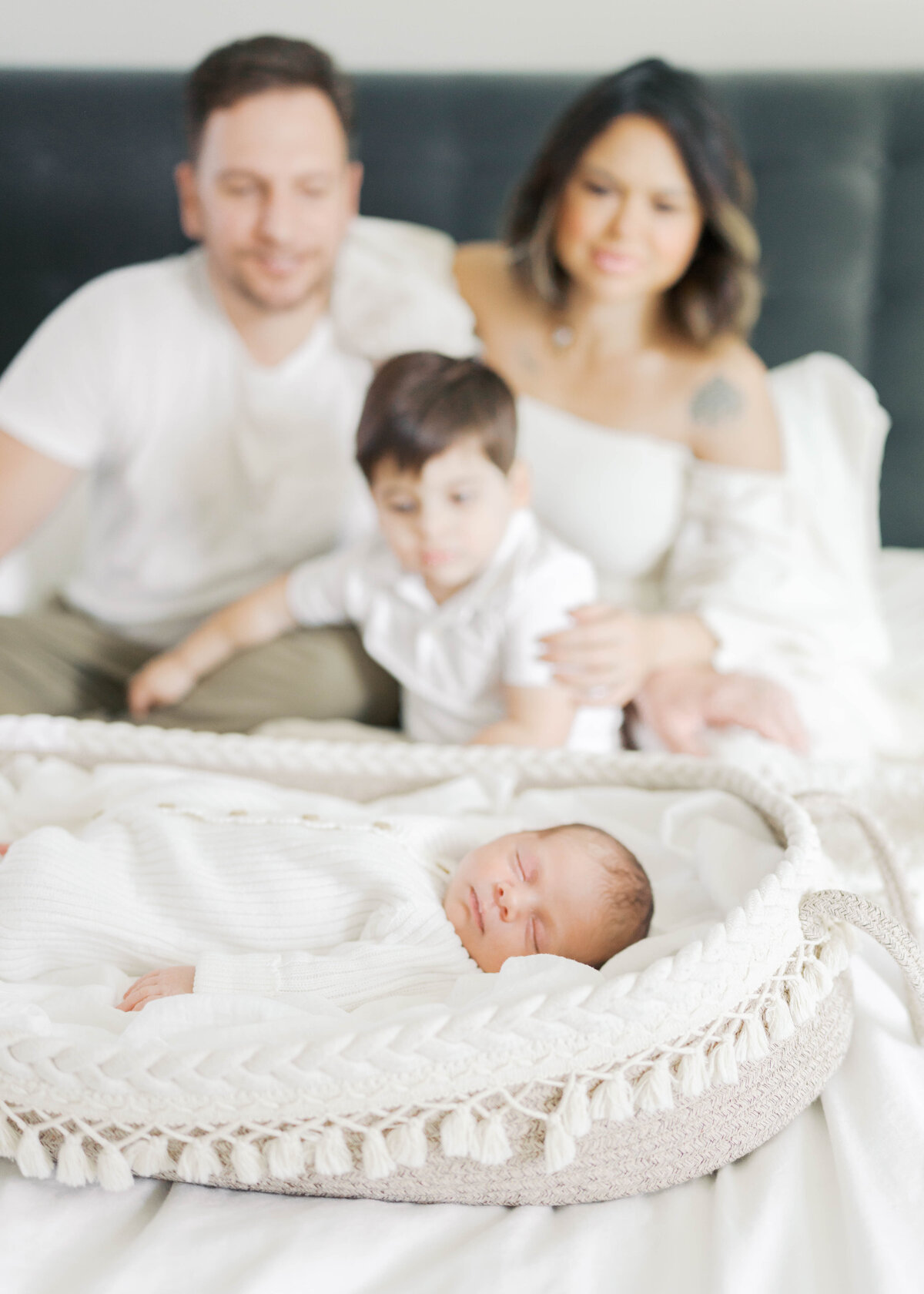 mom and dad and big sibling watching newborn baby brother sleep in moses basket in virginia beach newborn session
