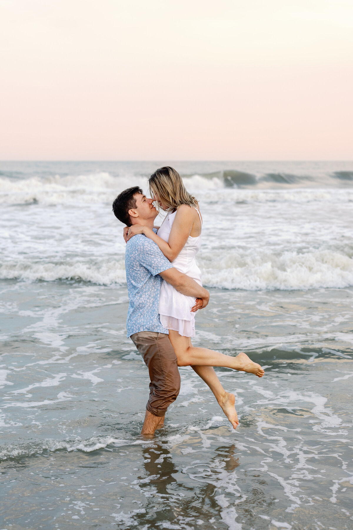 Man carrying his fiancée through shallow water, romantic Wilmington beach engagement