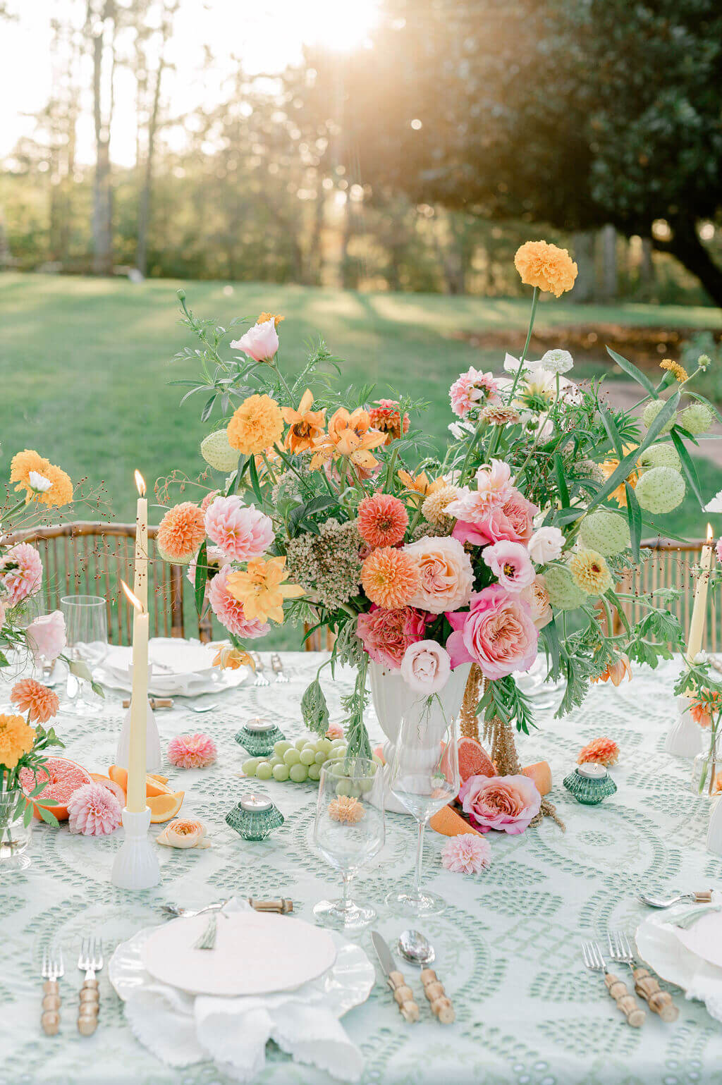 Vibrant outdoor wedding tablescape with lush florals, taper candles, and fruit accents.