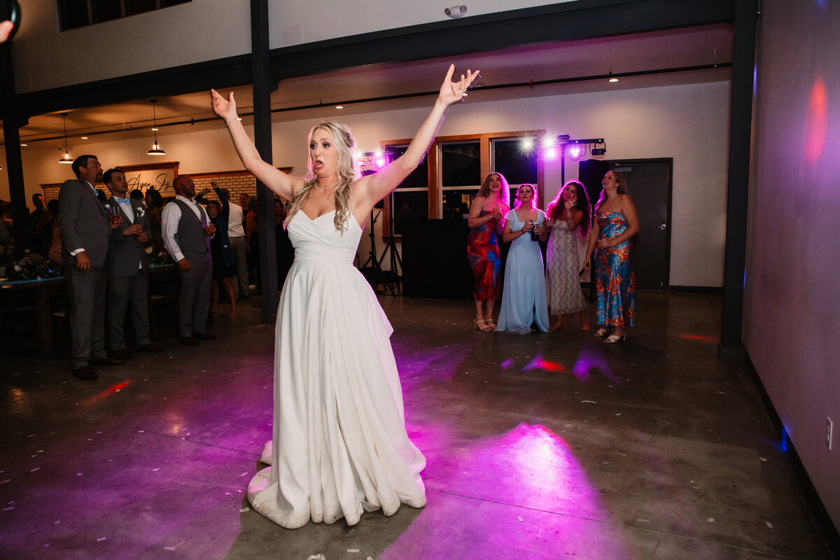 A bride dances alone on the dance floor with arms in the air