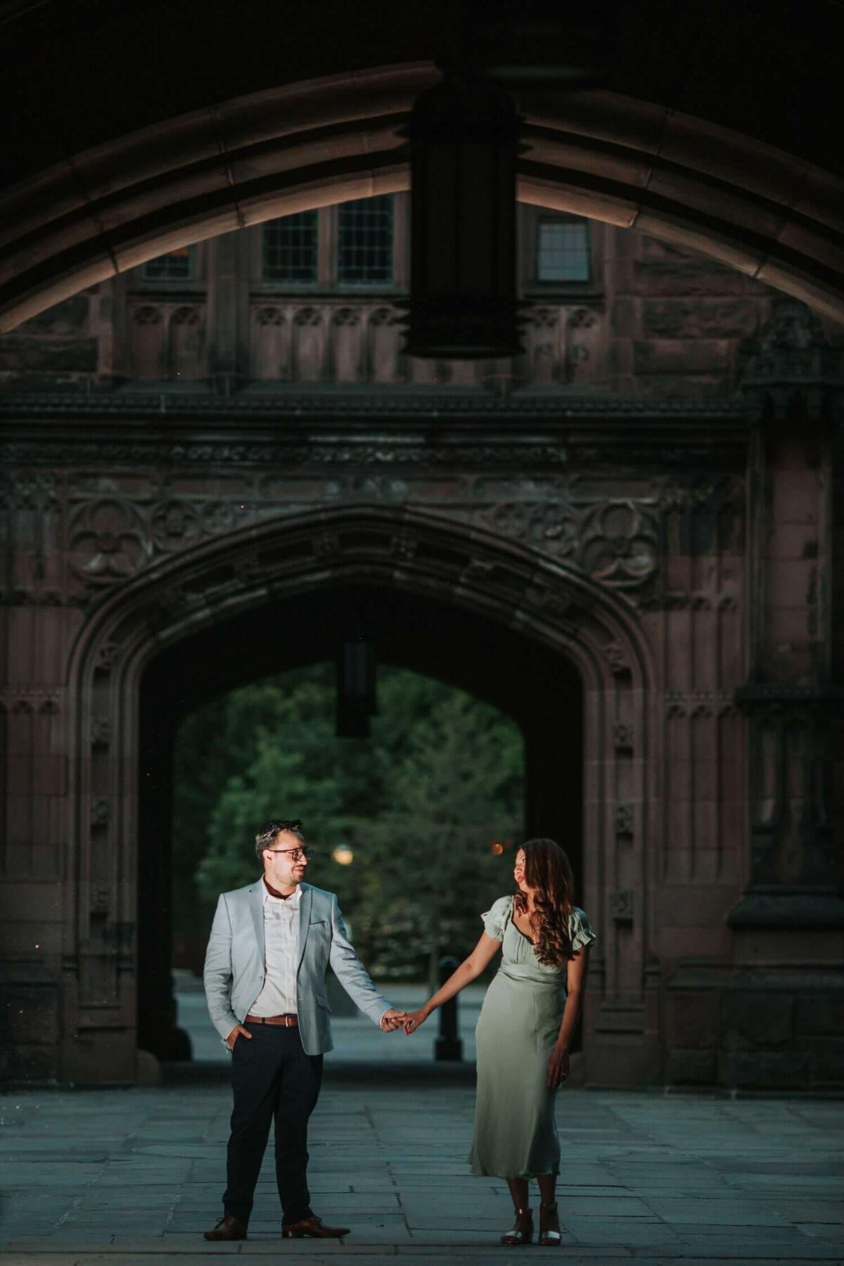 Couple holding hands standing in front of an arched walkway in Princeton New Jersey.