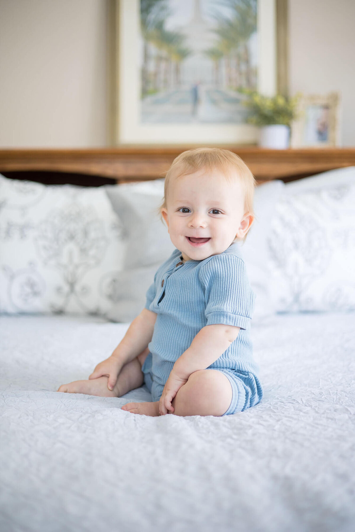 joyful one year old boy in blue sitting on a bed