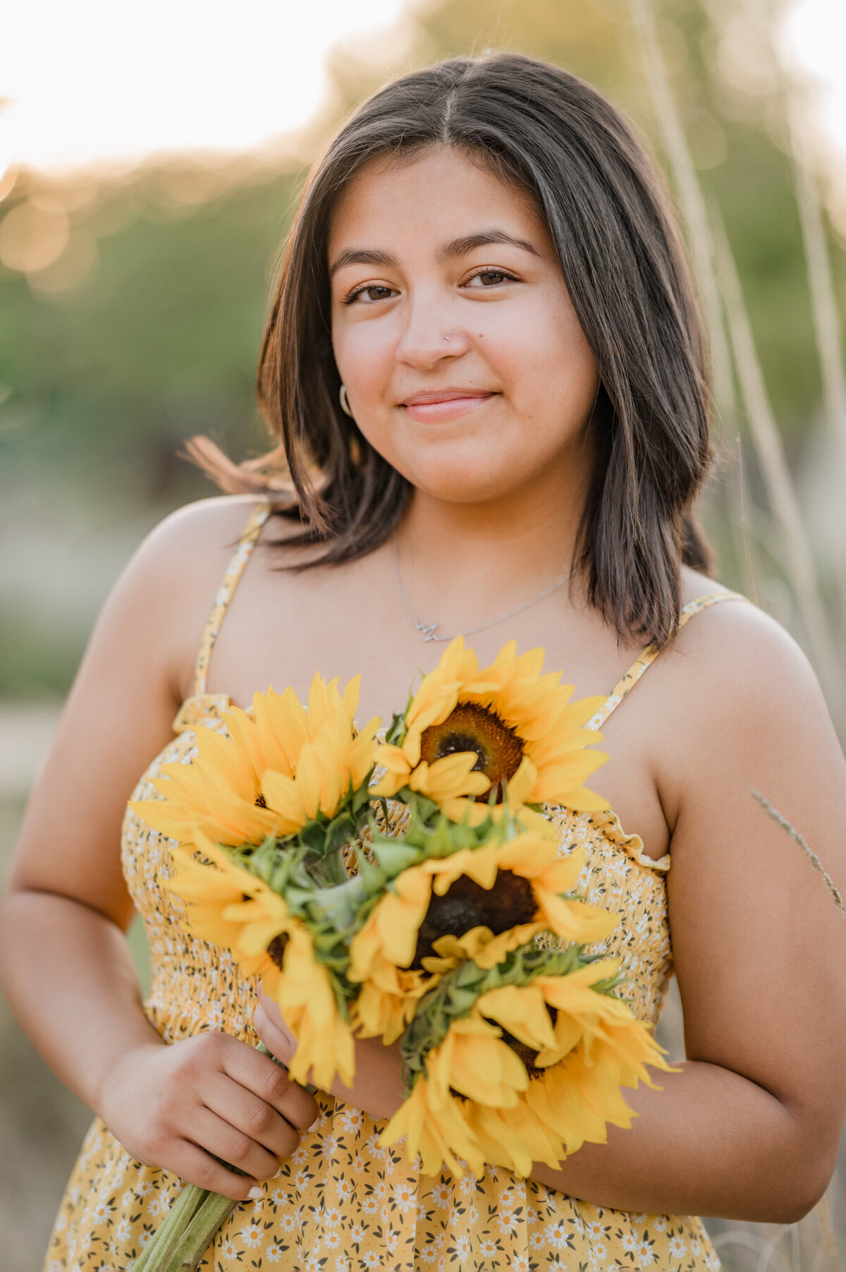 Senior portrait of a girl in a yellow dress holding sunflowers in golden hour.