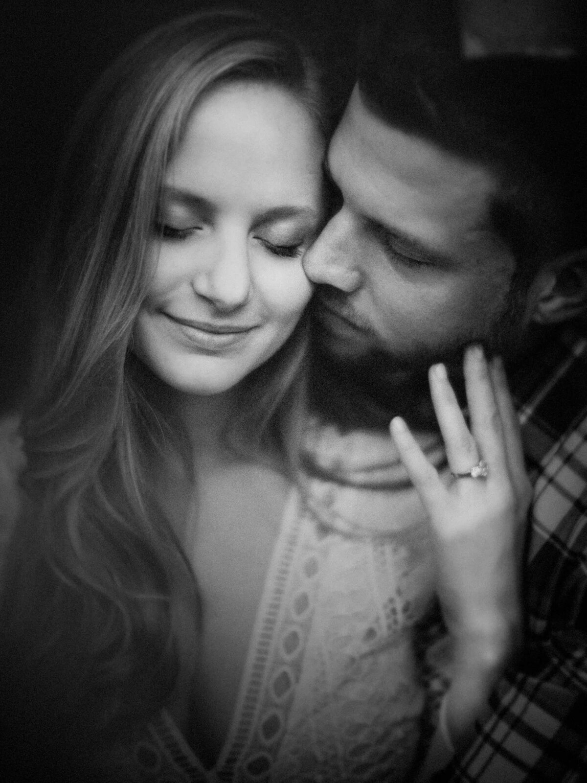 Intimate black and white portrait of a couple close together, with the woman showcasing an engagement ring