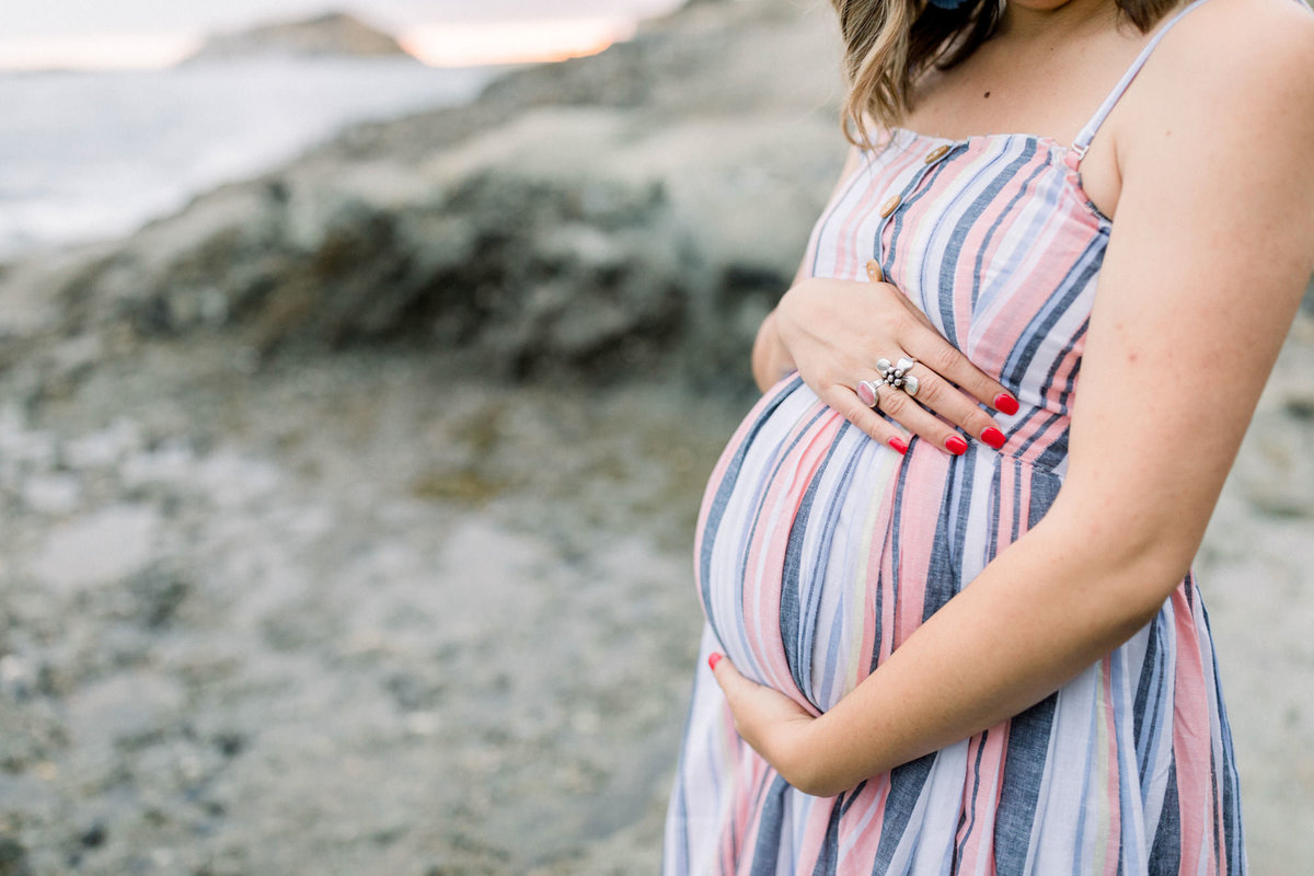 Expecting mother poses with her hands on her belly during a maternity session at the beach