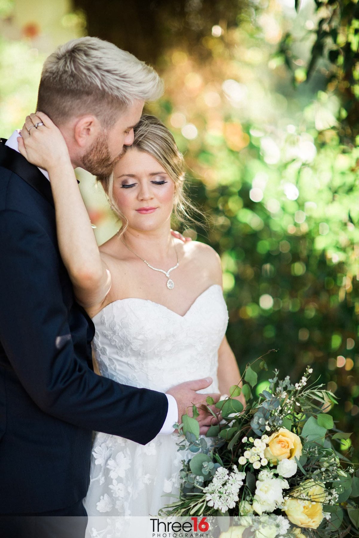Groom kisses his Bride's head as she closes her eyes and reaches up and holds him