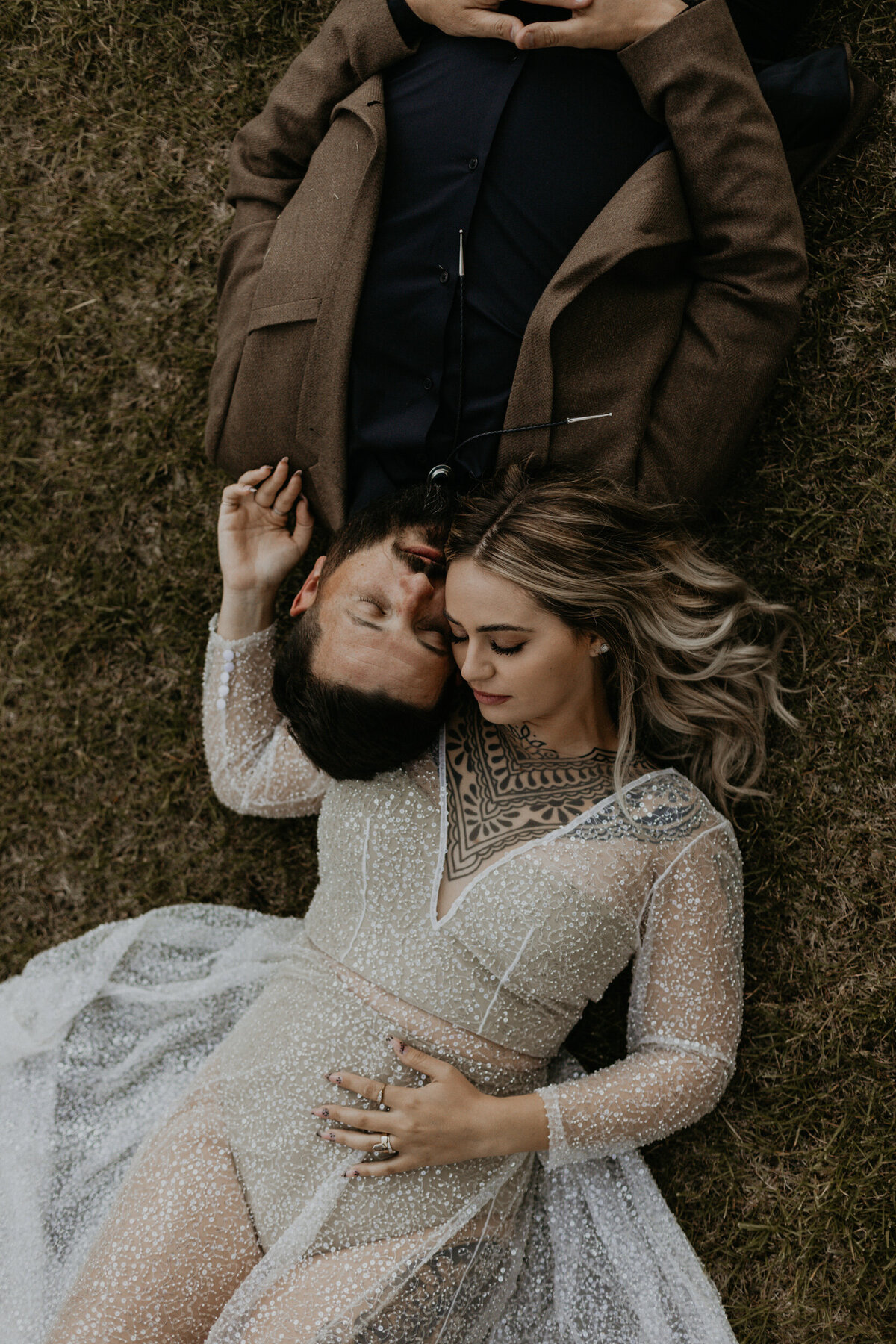 bride and groom laying together in grass wearing their wedding attire