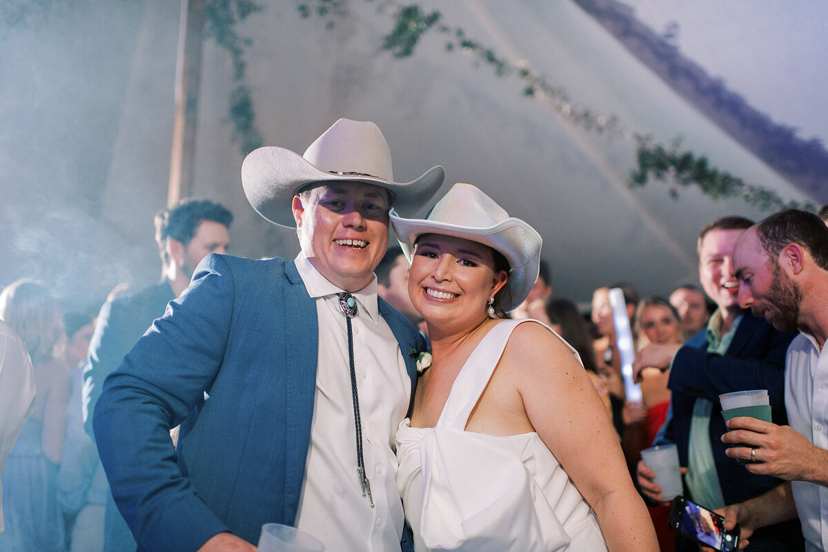  Bride and groom wearing cowboy hats smiling during a late-night reception party at a mountain wedding in Cashiers, NC.