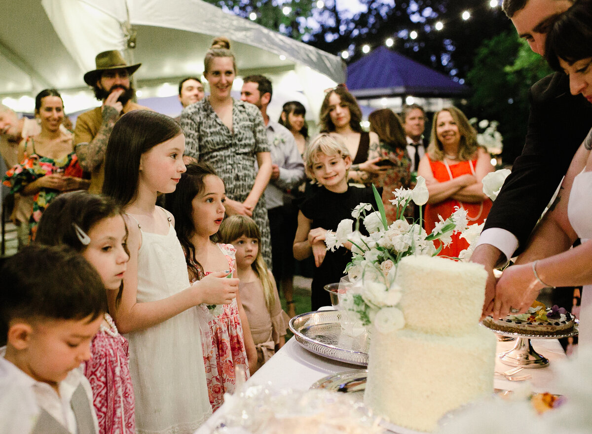 Bride and groom cutting wedding cake with children looking on at Umlauf Sculpture Garden, Austin