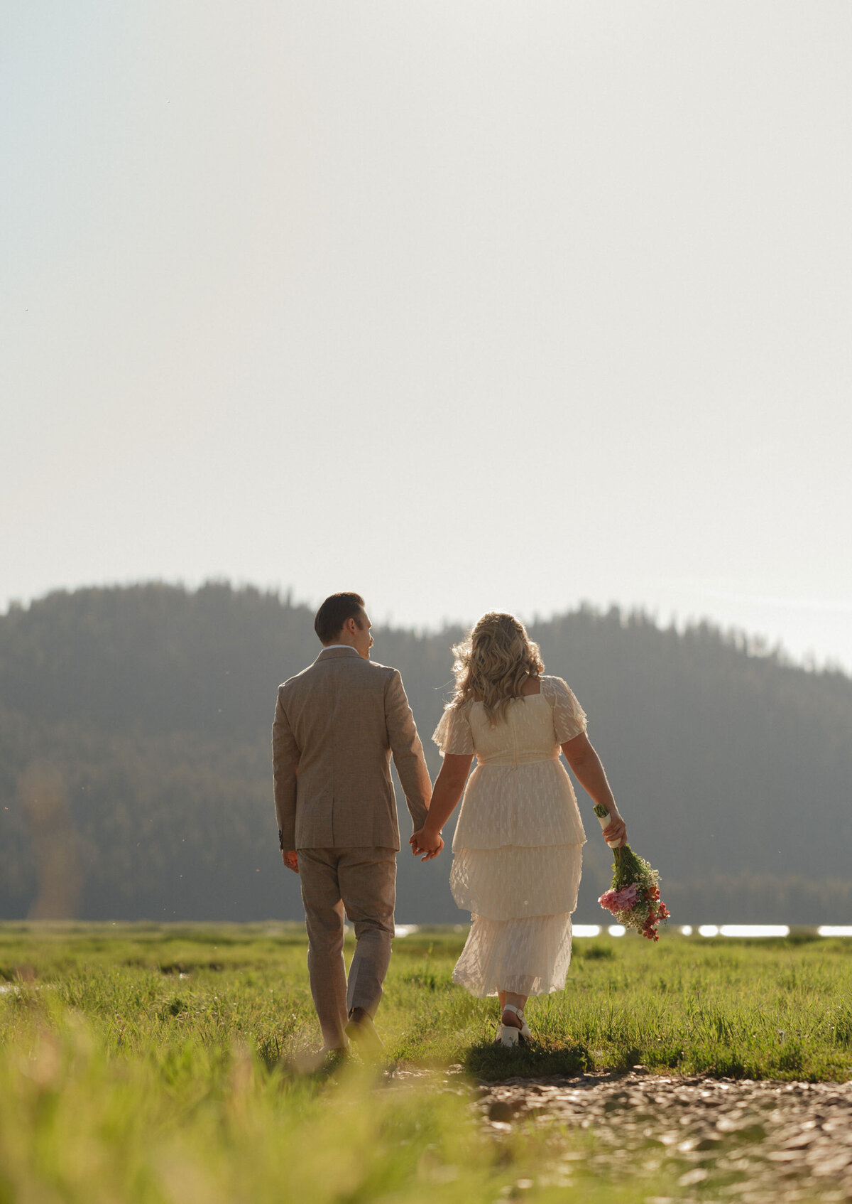 bride and groom walk off into the distance in an open meadow at Sparks Lake on a sunny glowing day