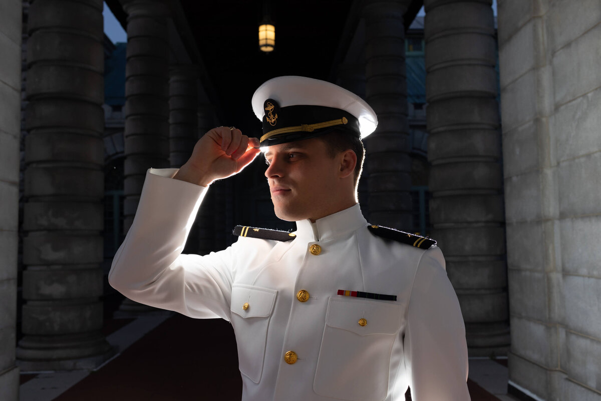 Backlit senior photo of Naval Officer in Whites on red beach at US Naval Academy in Annapolis, Maryland.