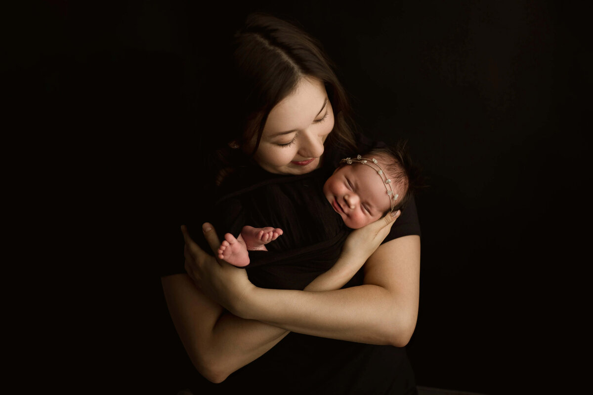 Mother cradling newborn against black background - intimate newborn portrait in studio 