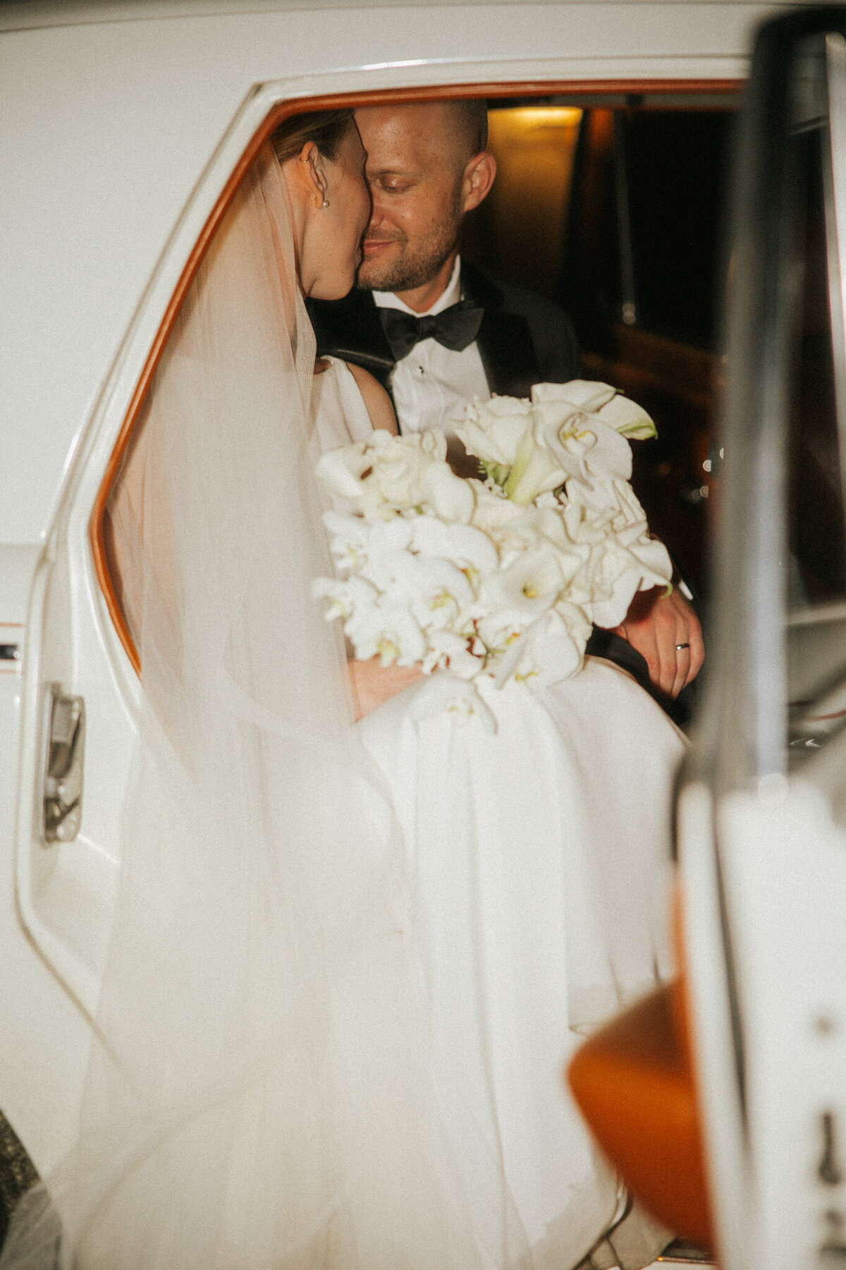 Couple sharing a kiss in a vintage car, captured on their special day.