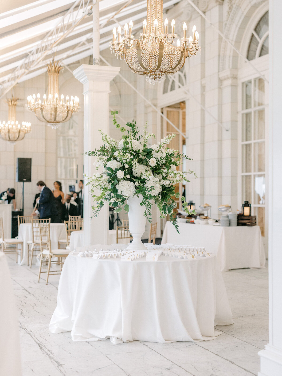 White round table with tall green and white centerpiece and wedding escort cards at Rosecliff Mansion in New England