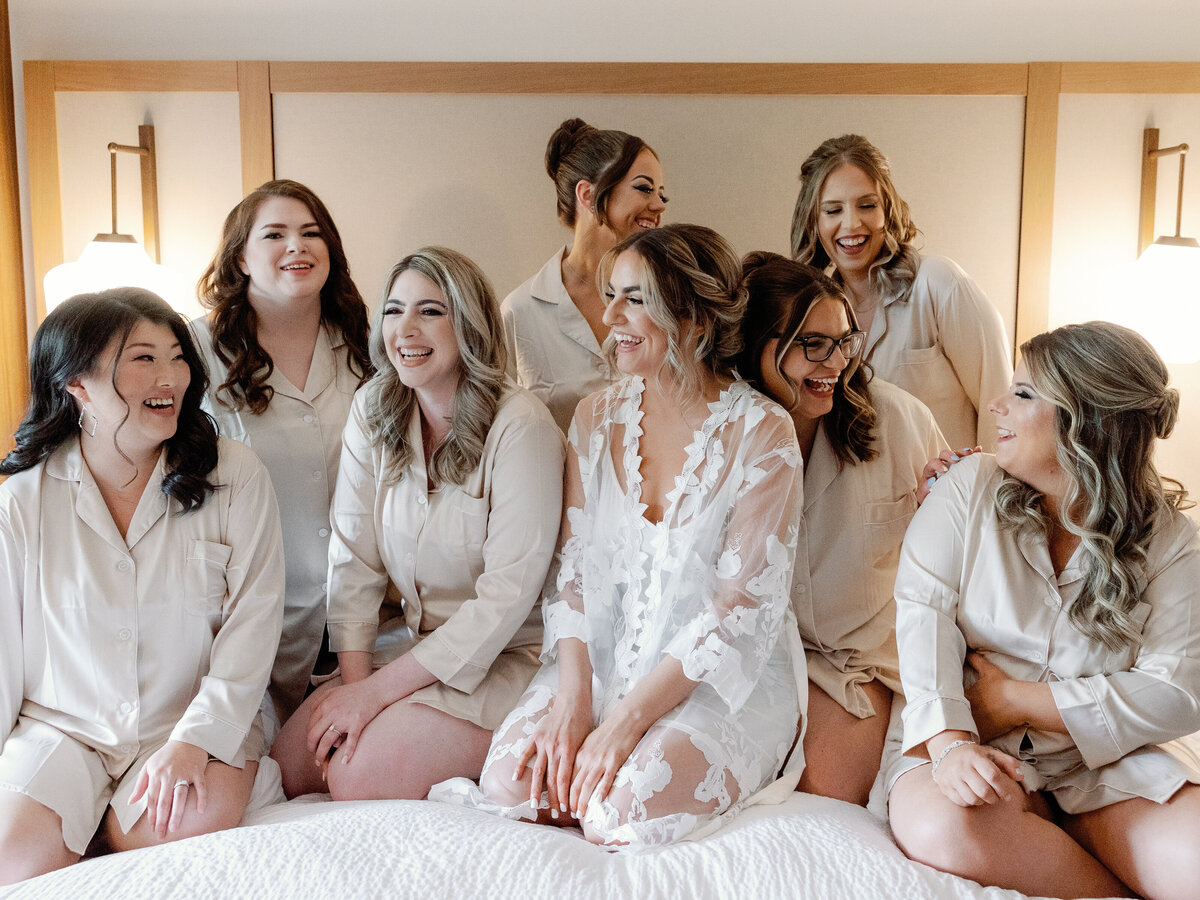 A bride enjoys her time with her bridesmaids as they all sit on a hotel bed and wear matching pjs