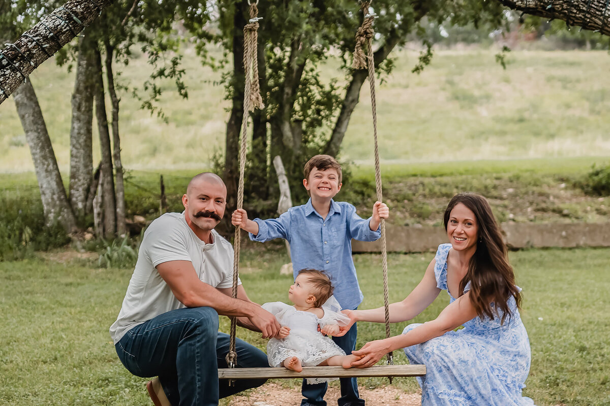 Little girl on swing with family seated around her during lifestyle session in New Braunfels, Texas.