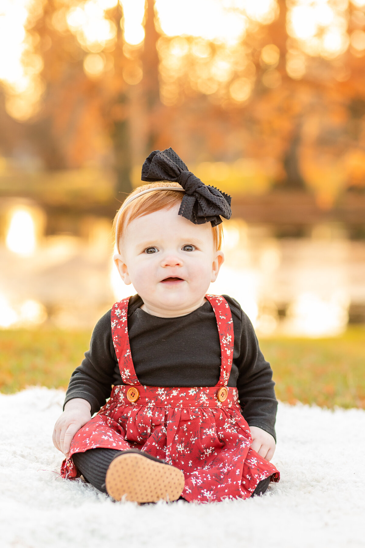 Baby girl sitting on blanket with golden Fall leaves and pond backdrop