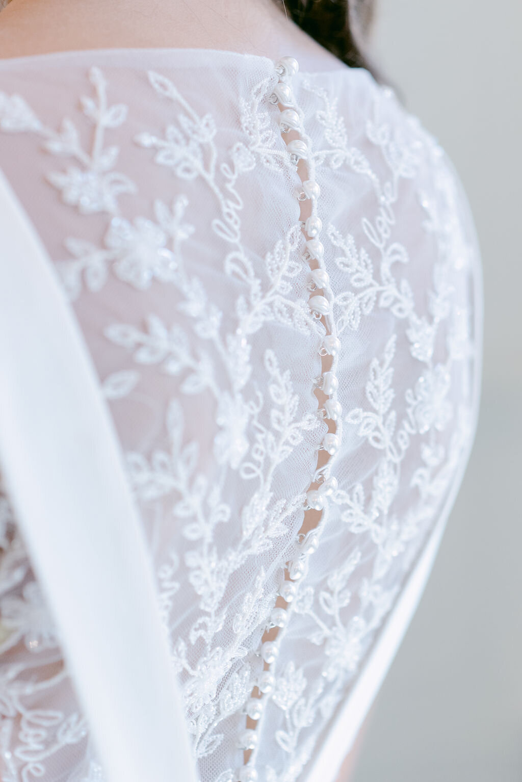 The beaded illusion back on the Jane crepe wedding gown features a custom floral and love embroidery and a pearl button closure.