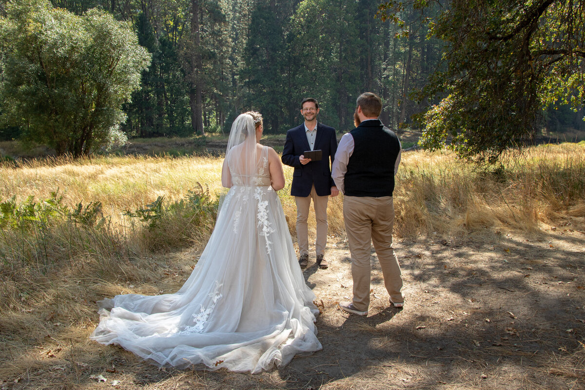 A bride and groom standing facing their officiant as he reads during their elopement ceremony.