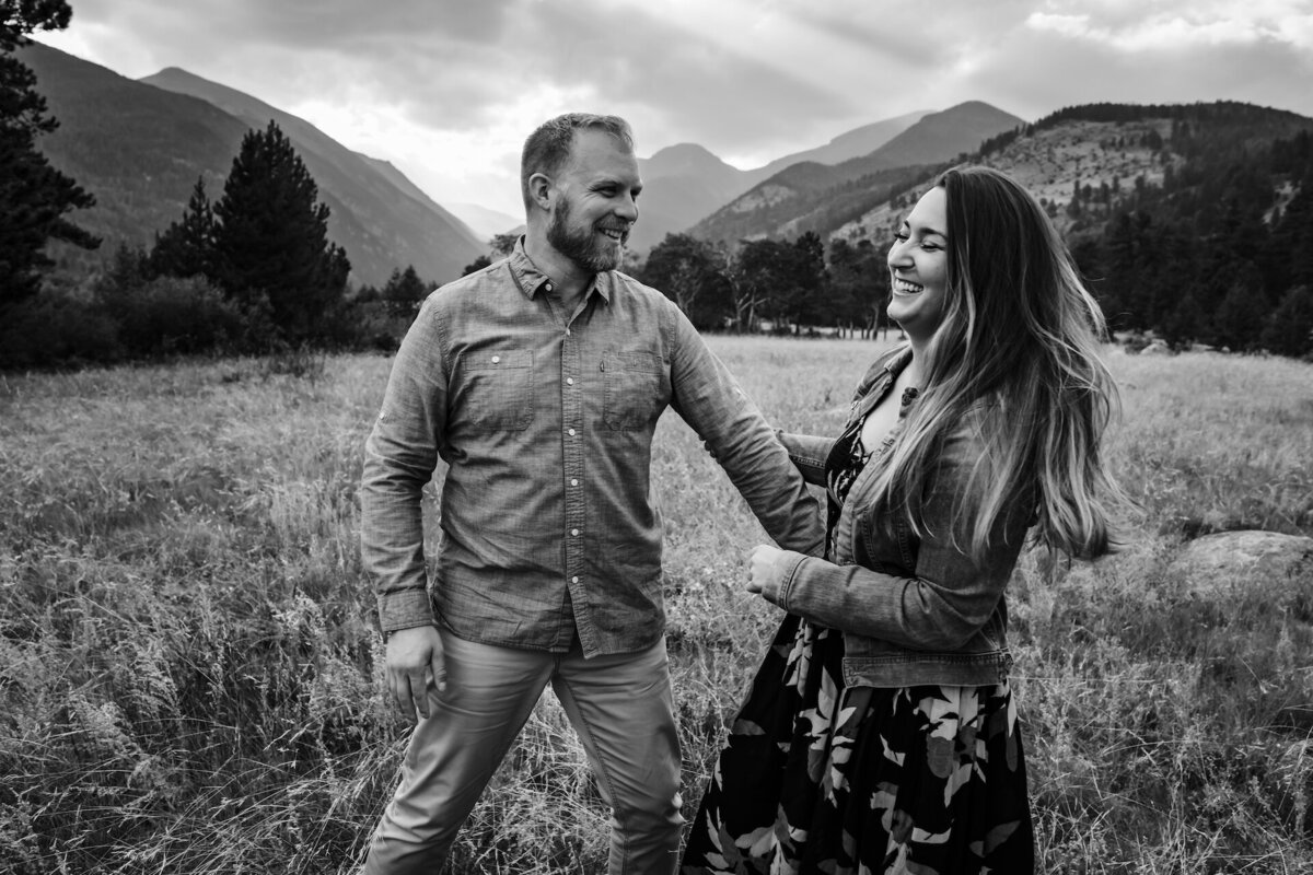 A couple laugh in a field with mountains in the back
