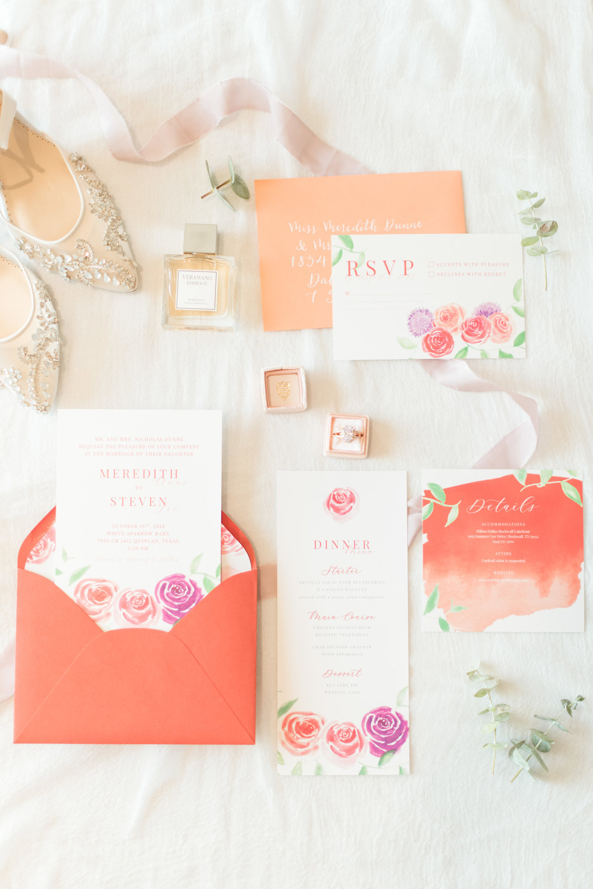Colorful orange wedding invitations displayed on table with bride's shoe, wedding ring box, and eucalyptus.