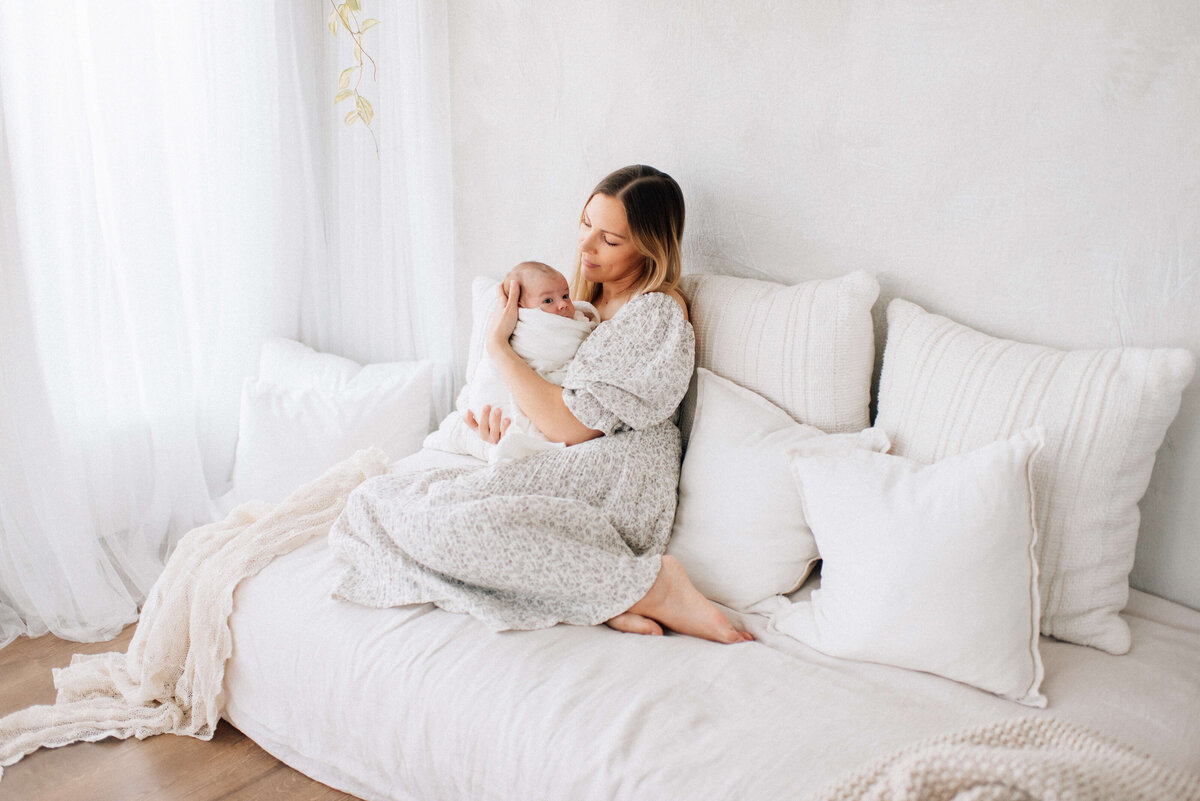 mother holding swaddled baby on a bed